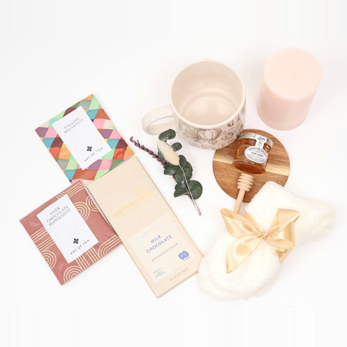 Flat lay of the fall tea gift box contents: mug, candle, honey, coaster, tea sachets, chocolate bar, and socks