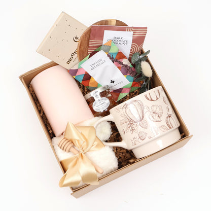 Cozy fall tea gift box with a pumpkin print mug, blush pillar candle, fuzzy socks, and honey in a kraft box