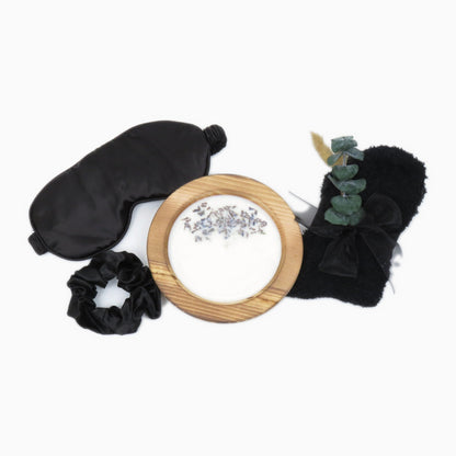 Black satin sleep mask, satin scrunchie, fuzzy knit socks, and lavender soy candle in a wood bowl