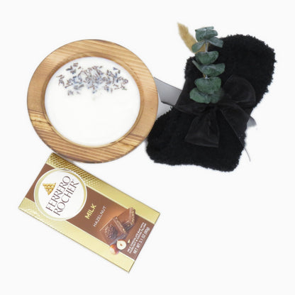 Lavender soy candle in a wood bowl with fuzzy knit socks and a milk chocolate hazelnut bar