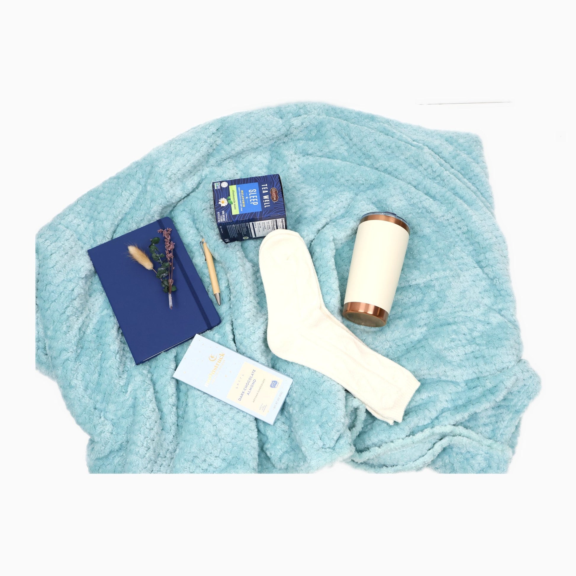 Contents of the sleep and relaxation gift box spread on the plush aqua throw