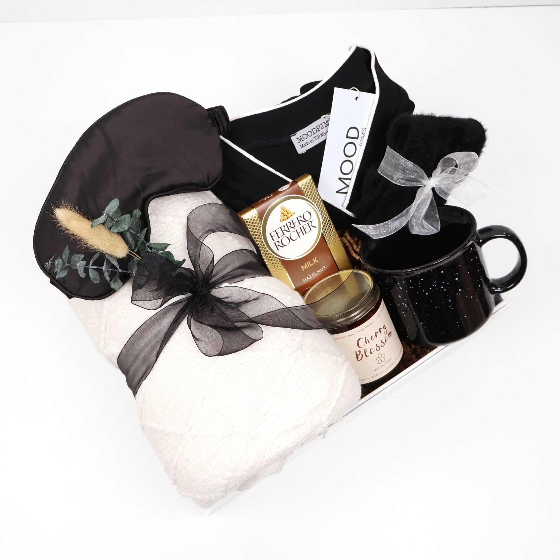 Elegant sleep and loungewear gift box for her with black pajama set, quilted cream throw, ceramic mug, candle, and eye mask